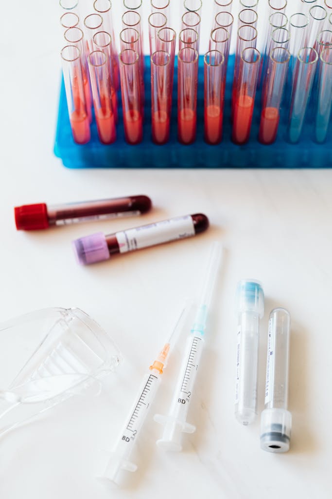 From above of transparent test tubes with colorful liquids placed on blue stand and table near syringes and plastic eyeglasses