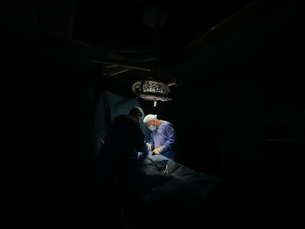 Two surgeons focus intently on a medical operation under surgical lights.
