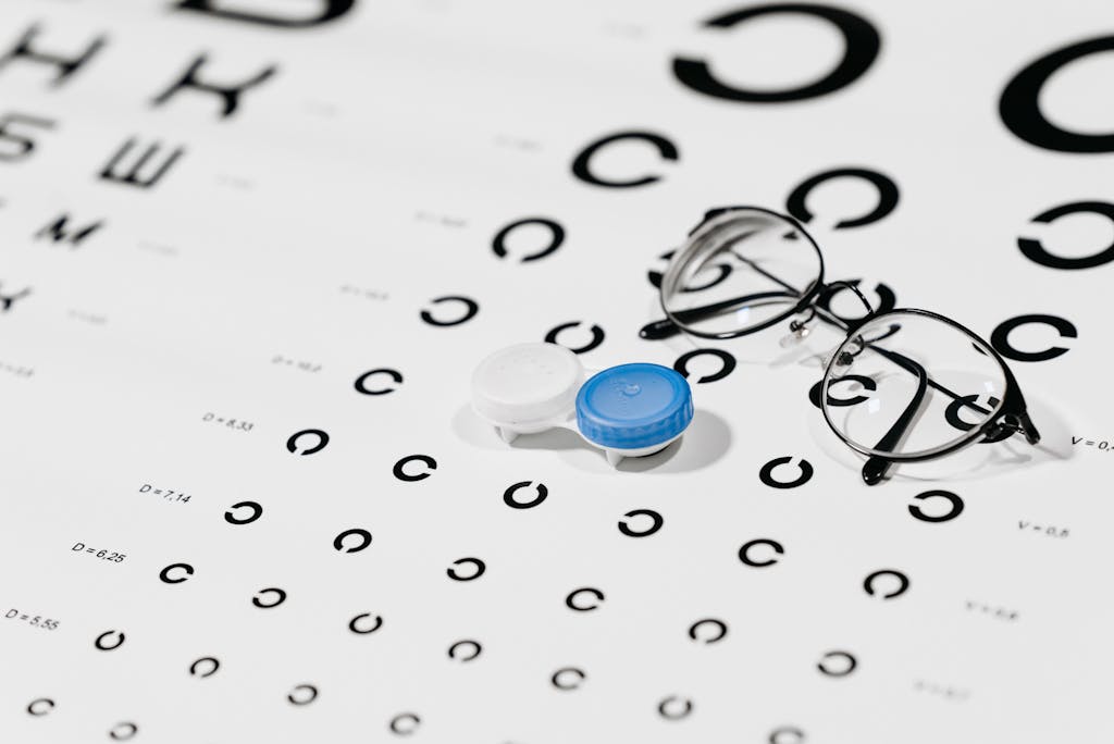 Close-up of contact lens case and eyeglasses on an eye test chart, ideal for vision care concepts.