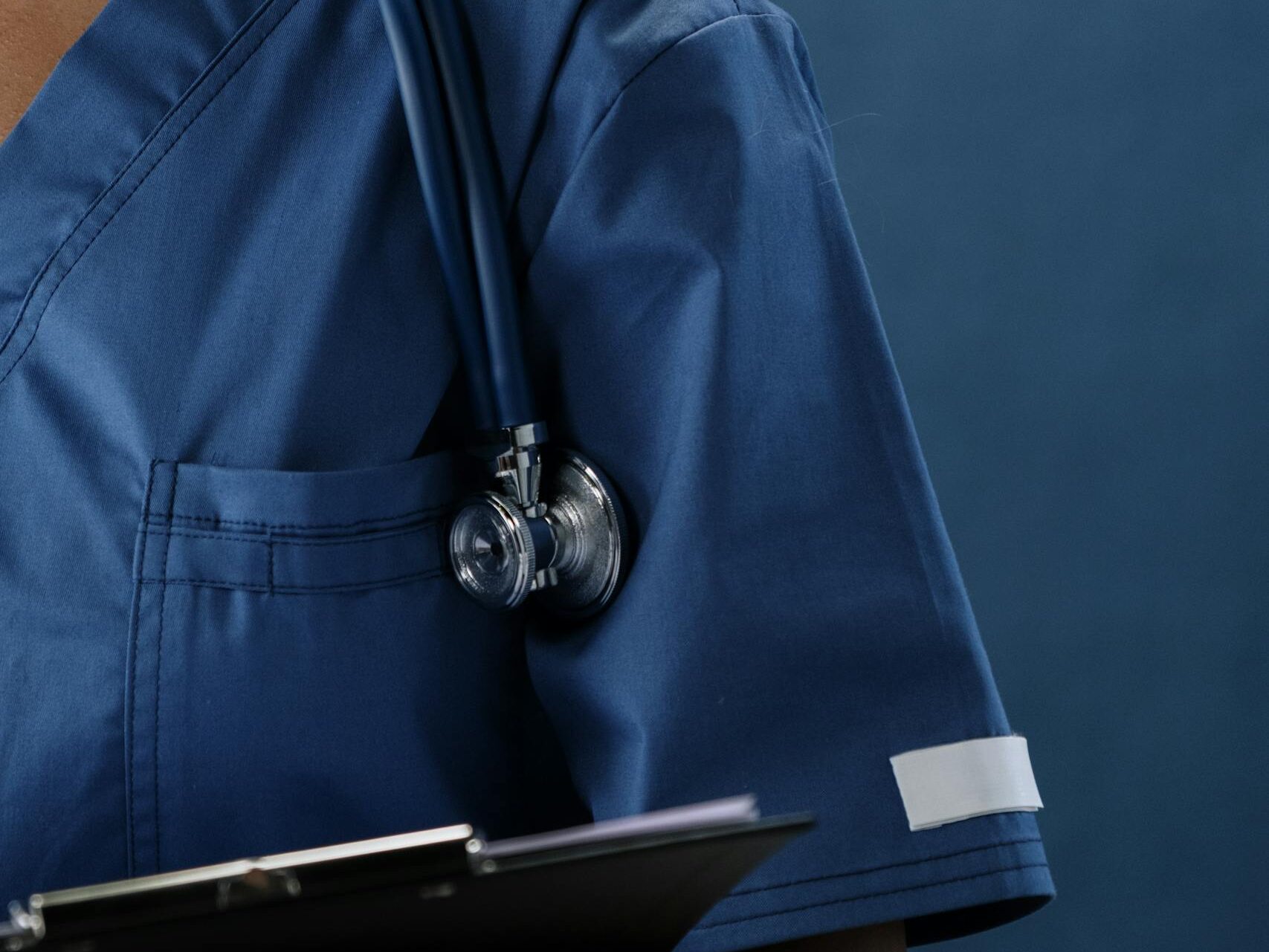 Close-up of a healthcare professional in blue scrubs with a stethoscope and clipboard.