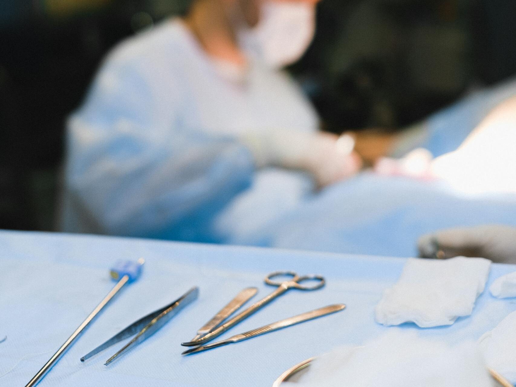 Focused surgeon in sterile operating room setting with surgical tools in foreground.