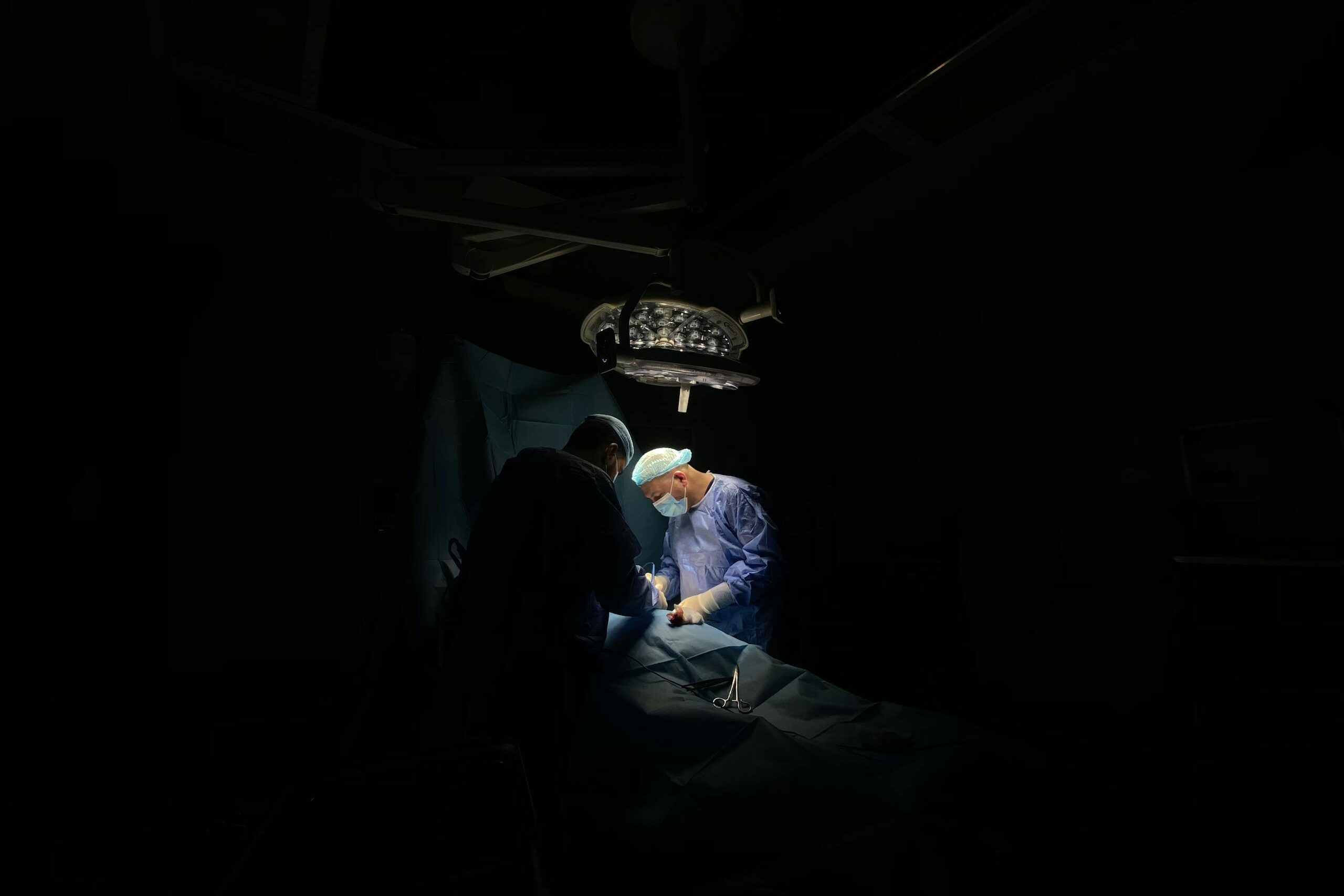 Two surgeons focus intently on a medical operation under surgical lights.